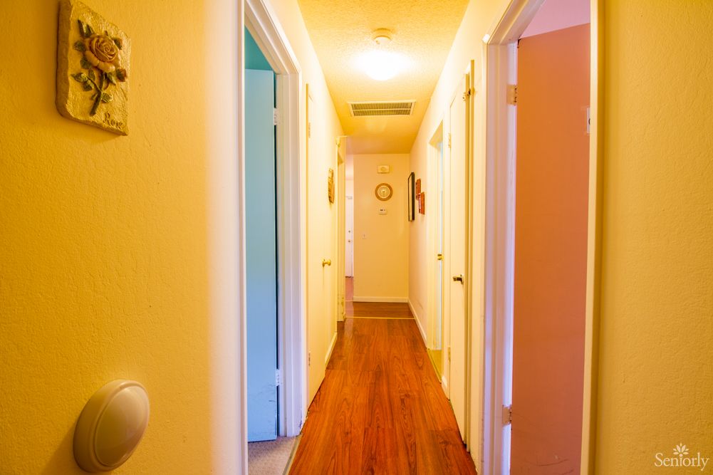 A brightly lit hallway with multiple doors and a wooden floor.