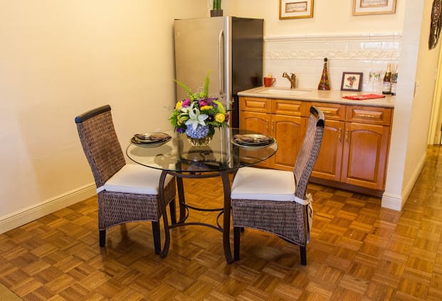 A cozy dining area with a glass top round table and wicker chairs, featuring a floral centerpiece.
