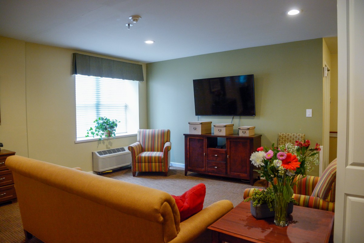 A cozy living room with a sofa, armchair, and a TV mounted on the wall.