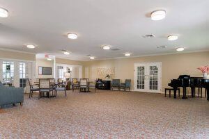 A spacious interior room with tables and chairs arranged neatly, featuring carpet flooring and overhead lighting.