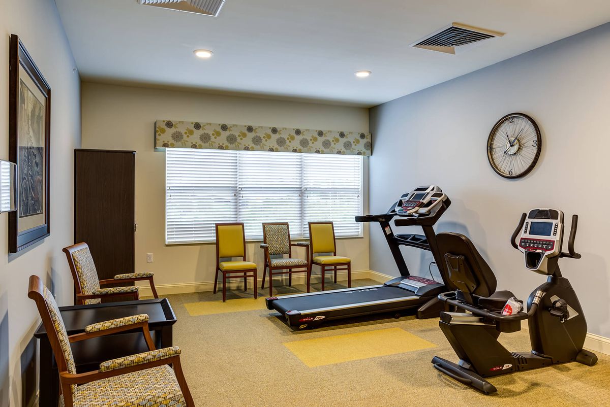 A small exercise room with a treadmill, chairs, and a large window.