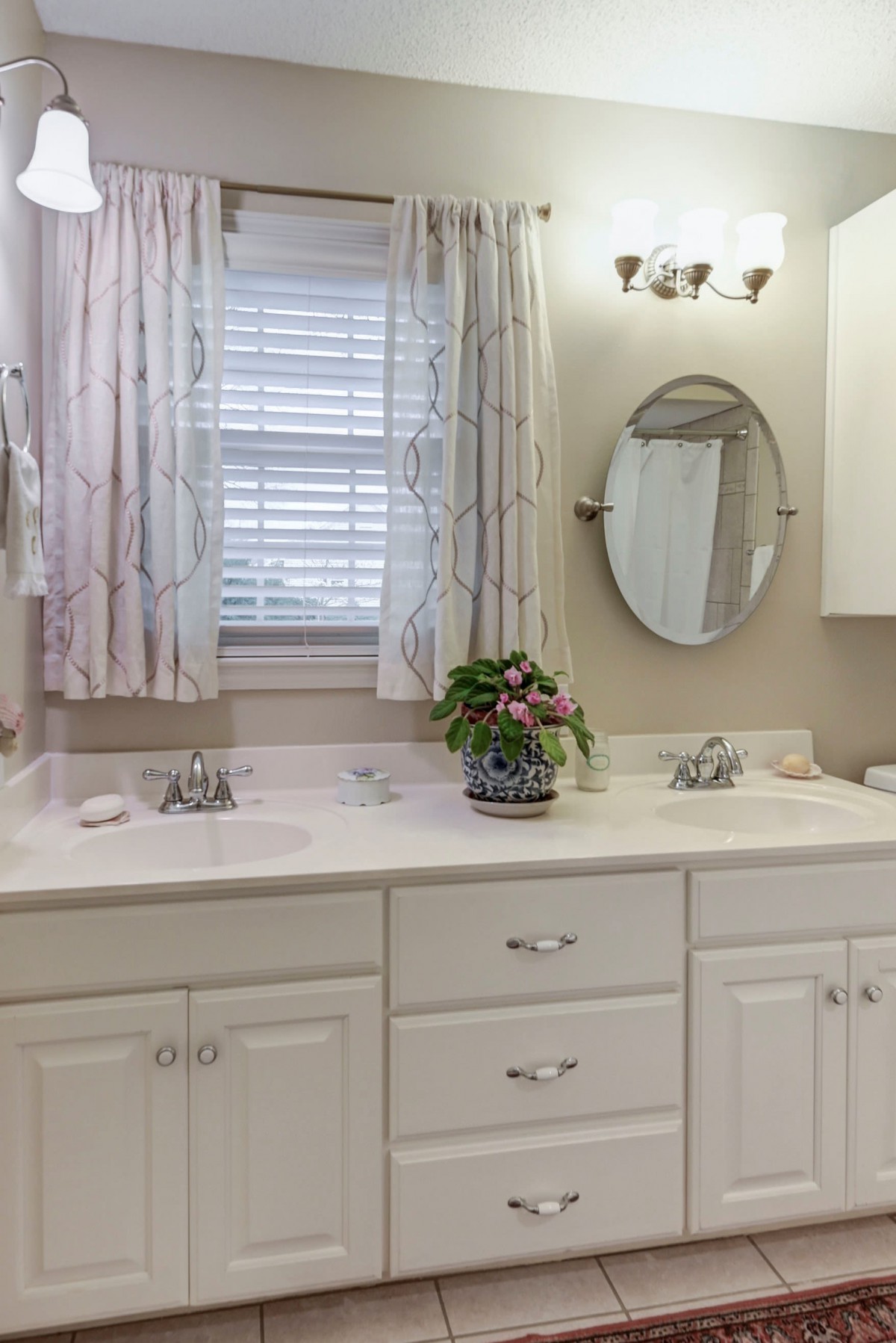A clean and bright bathroom featuring double sinks, a round mirror, and elegant light fixtures.