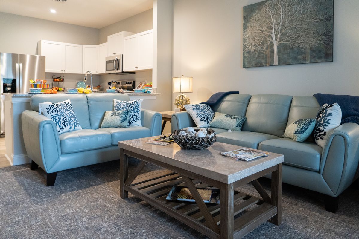 A cozy living room with a modern open-concept kitchen, featuring light blue sofas, a wooden coffee table, and decorative elements.
