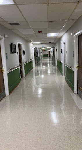 A wide view of a hospital corridor with multiple doors leading to patient rooms.
