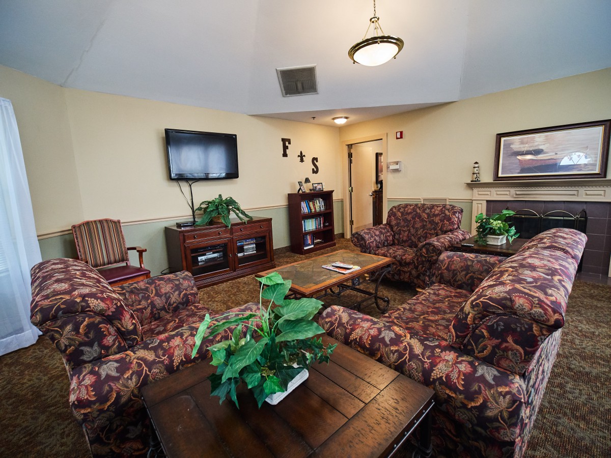 A cozy living room with patterned sofas, a television, and indoor plants.