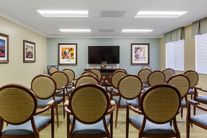 An empty meeting room with rows of chairs facing a large television and framed artworks on the walls.