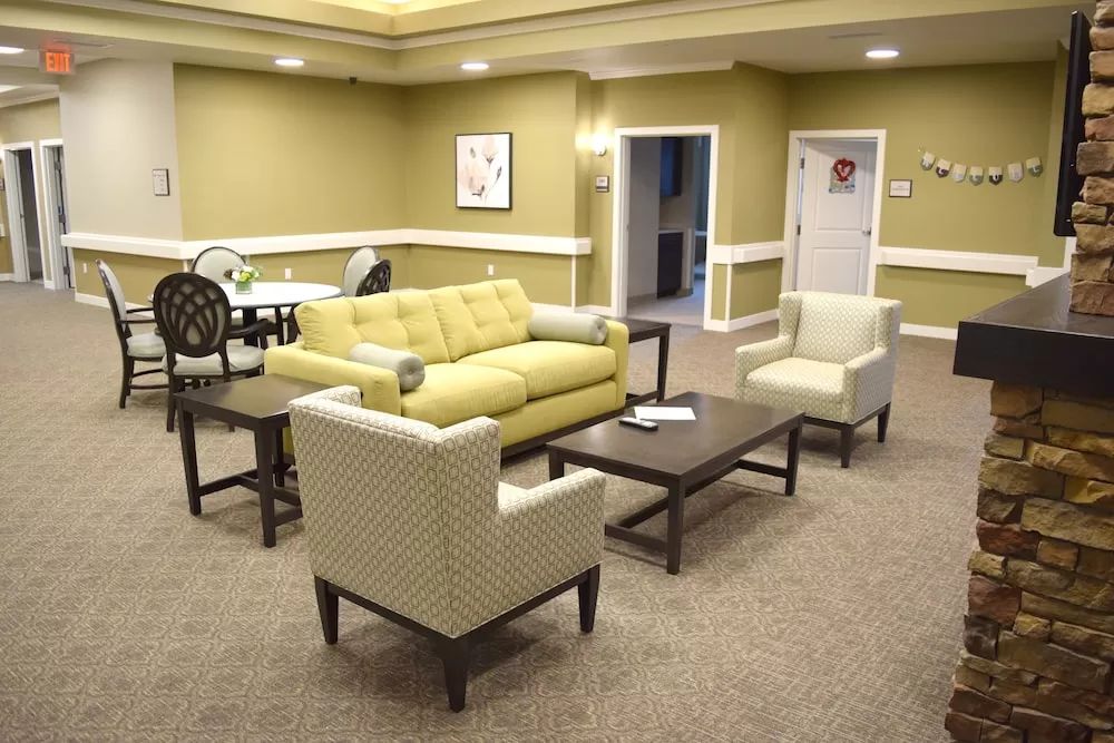A modern living room with a sofa, armchairs, and coffee tables arranged on a carpeted floor.