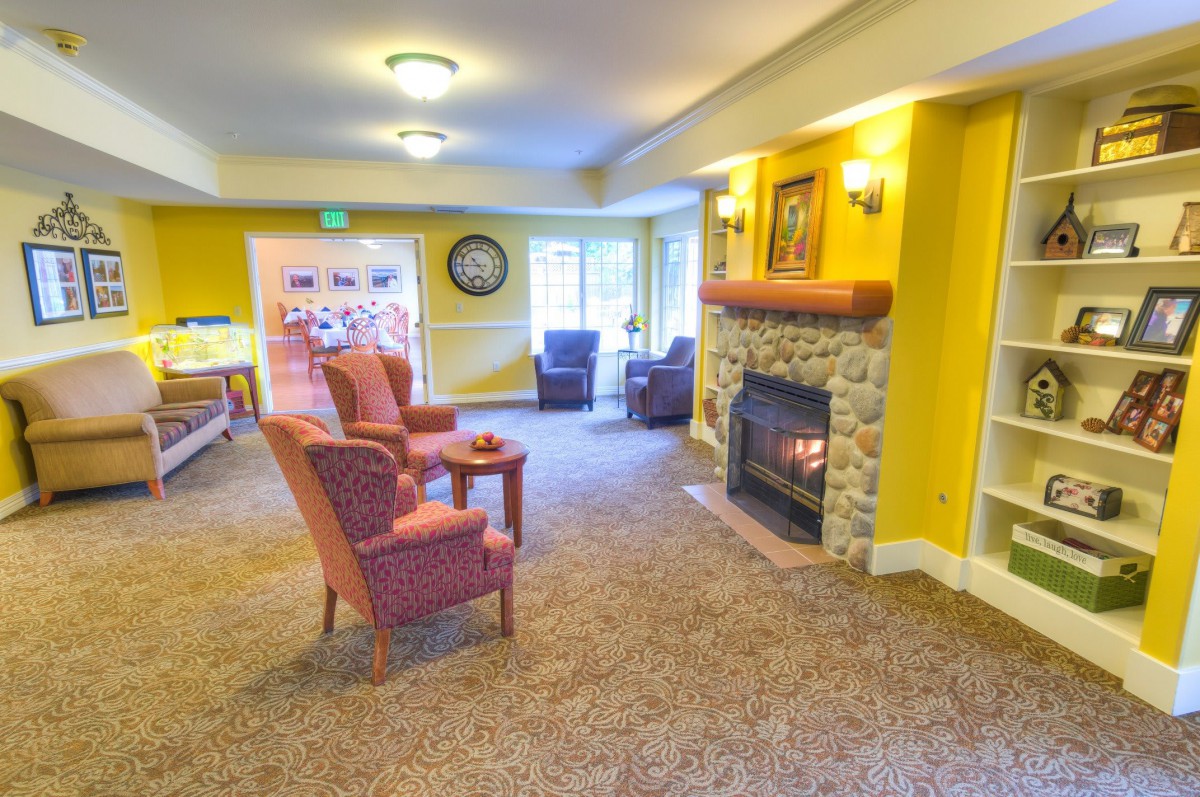 A cozy living room with armchairs facing a stone fireplace and carpeted flooring.