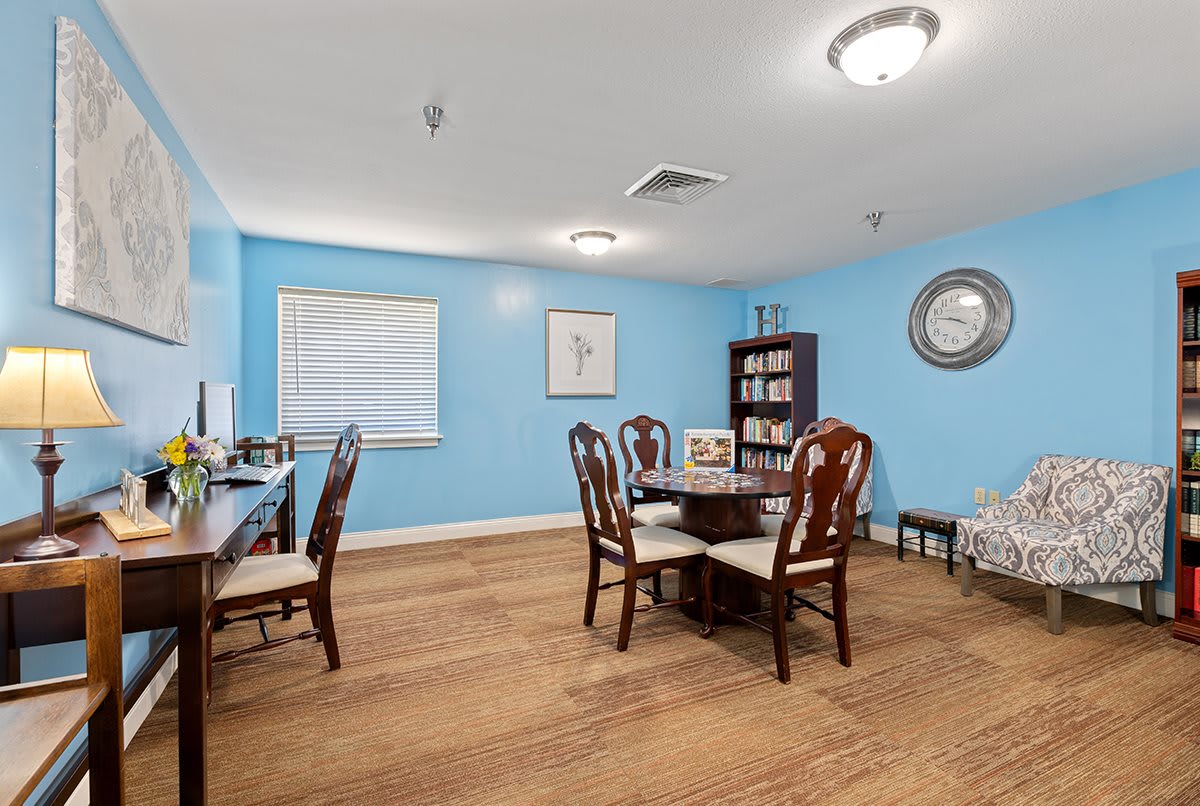 A well-organized office space featuring a round table with chairs, a desk with a computer, and a bookshelf against blue walls.