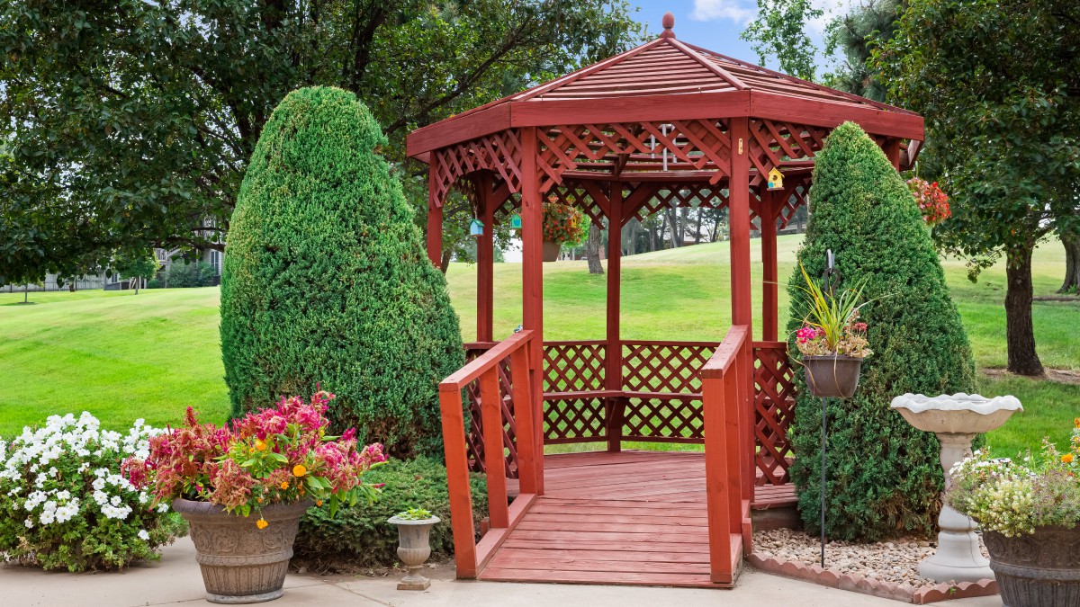 A charming wooden gazebo nestled in a beautifully maintained garden with lush greenery.