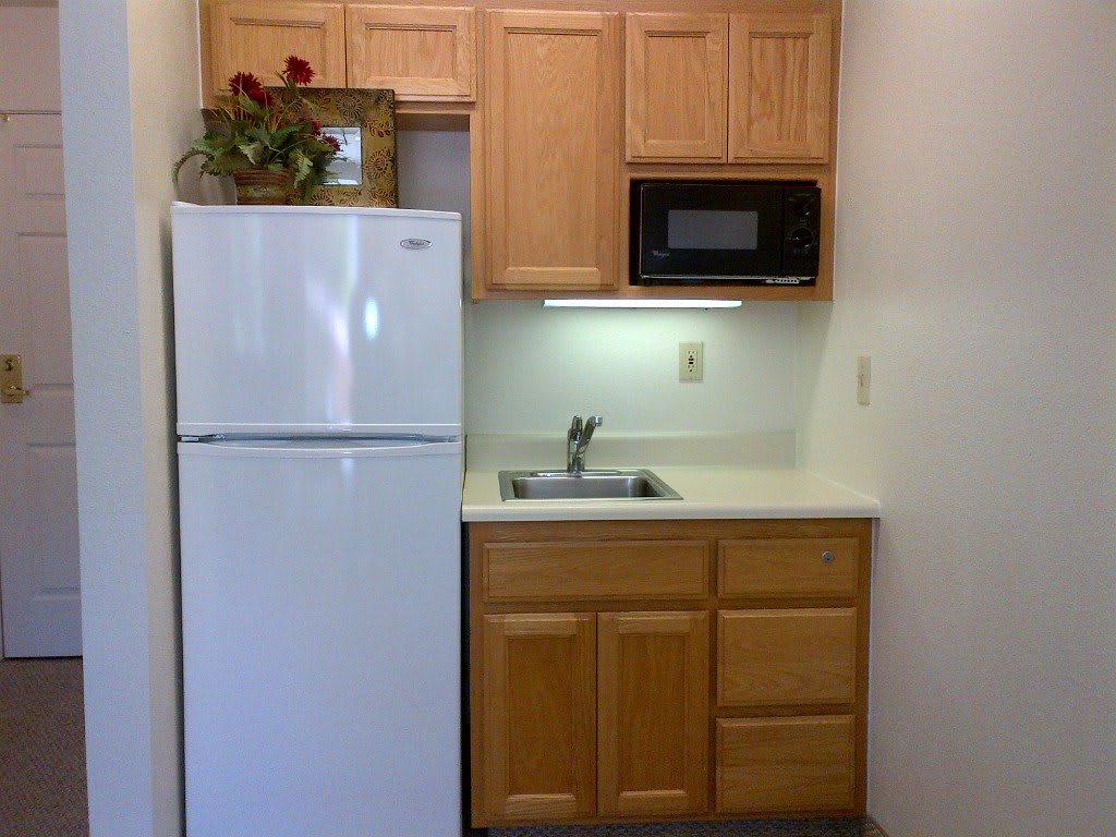 A compact kitchen area with wooden cabinets, a refrigerator, microwave, and sink.