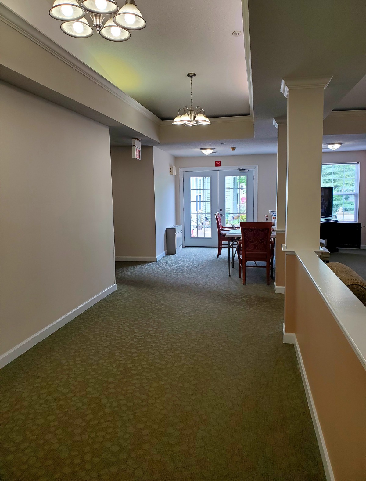 A bright hallway leading to a dining area with large windows and a carpeted floor.