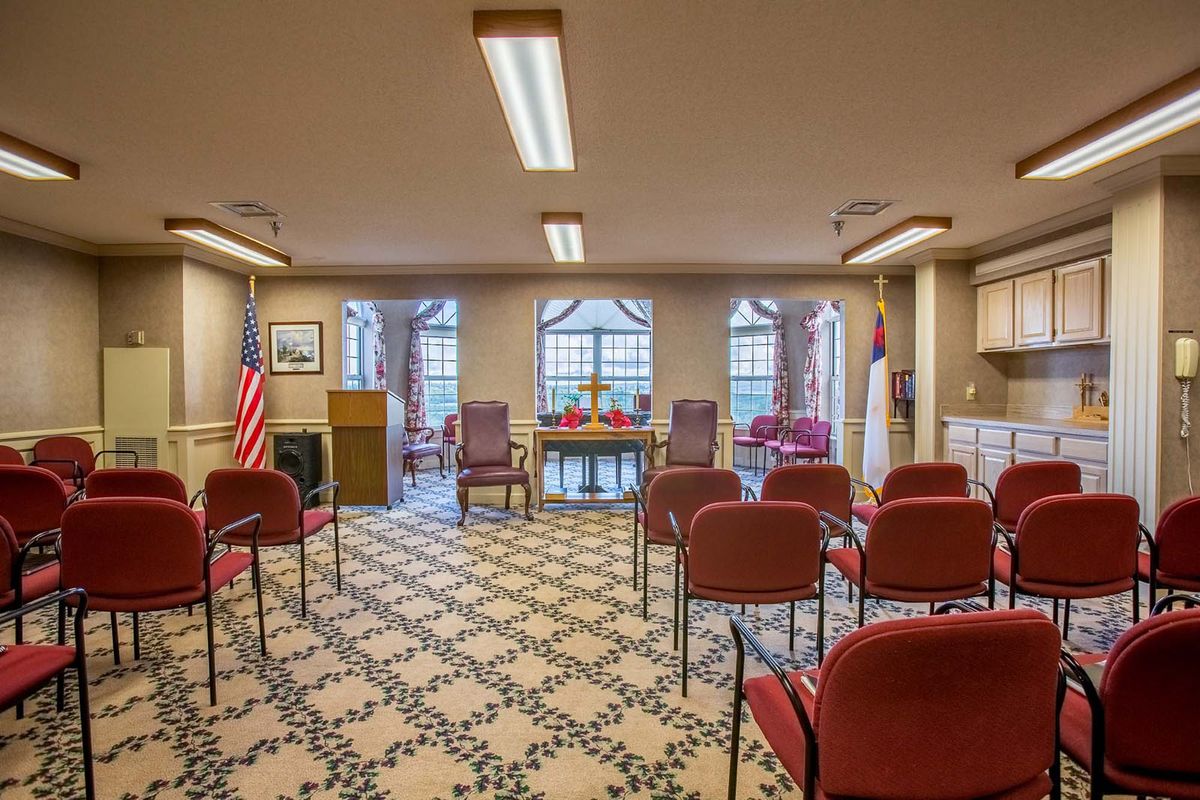 A small room set up for a ceremony with chairs, flags, and large windows.