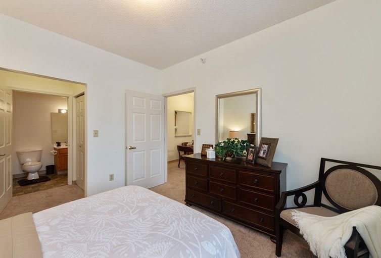 A neatly arranged bedroom with a bed, dresser, mirror, and chair.