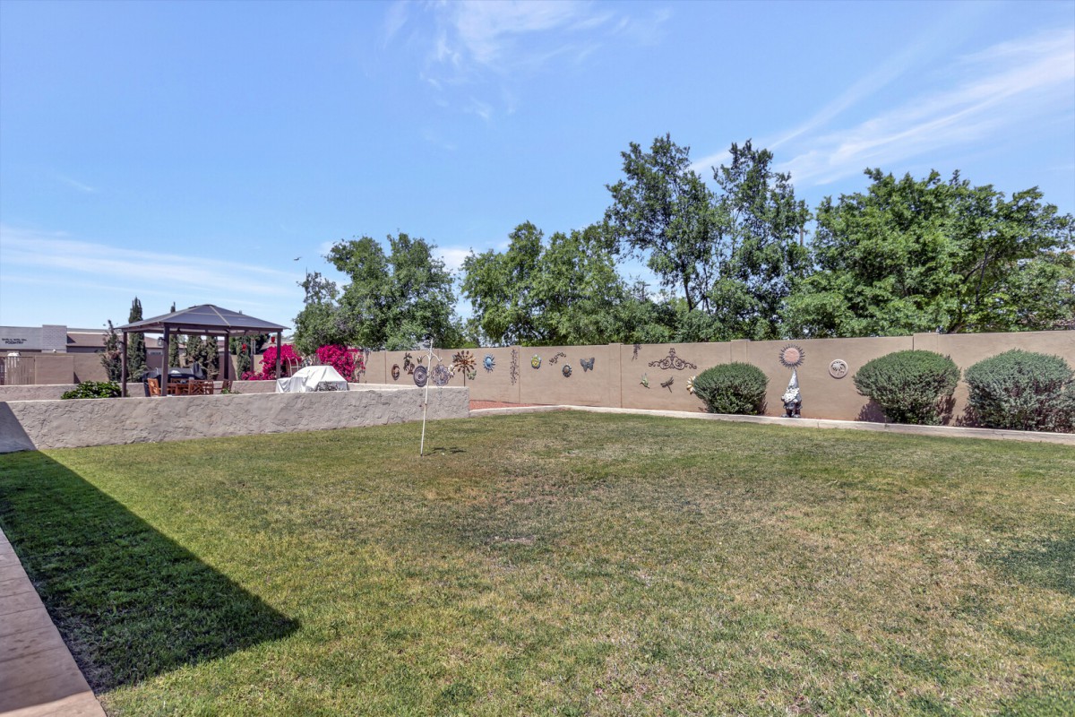 A spacious backyard with a well-kept lawn, featuring a playground and gazebo alongside trees and a fence.
