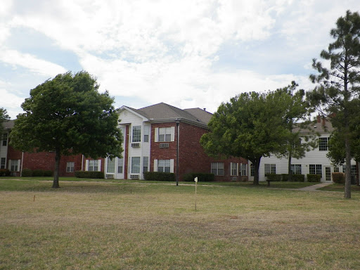 An apartment complex surrounded by green grass and trees under a cloudy sky.