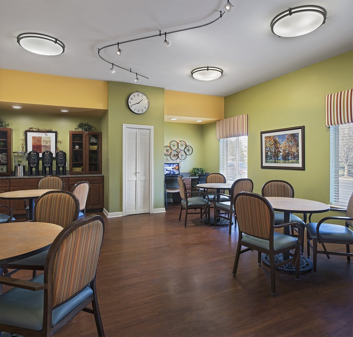A cozy dining area with multiple tables and chairs, featuring green walls and wooden flooring.