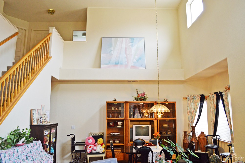 A cozy living room with high ceilings, featuring a bookshelf, dining table, and various decorations.
