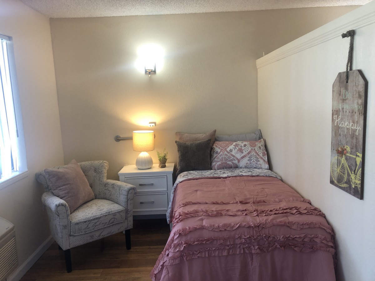 A cozy bedroom with a single bed, nightstand, and a comfortable chair.