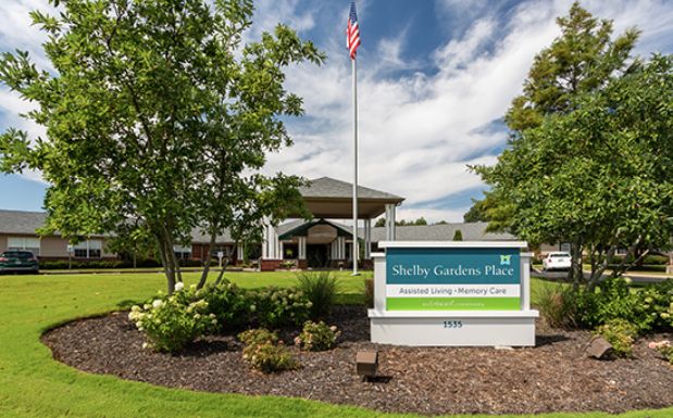 Front view of a building with landscaped garden and a sign at the entrance under a cloudy sky.