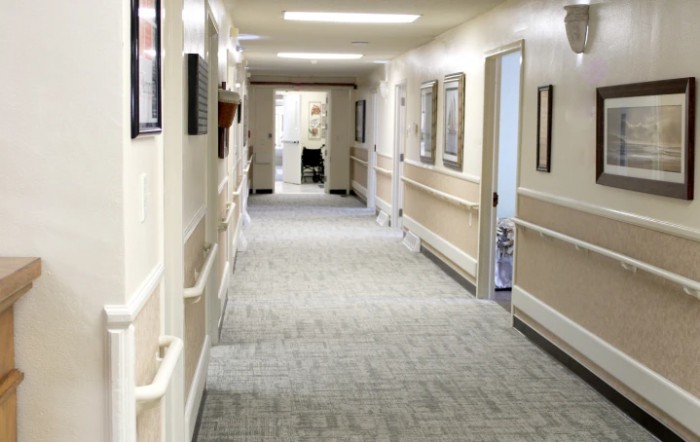 An empty hallway in a healthcare facility, featuring neutral-colored walls and bright lighting.