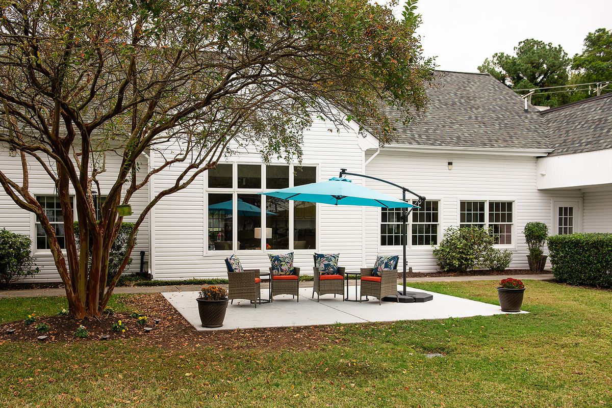 A cozy backyard patio area featuring outdoor furniture and a bright blue umbrella, surrounded by well-maintained landscaping.