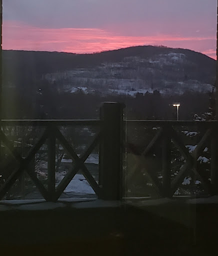 A serene winter sunset over the mountains, framed by a rustic railing.