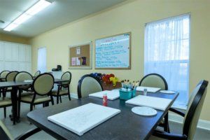 A well-lit room set up for an art workshop, featuring tables with chairs and various art supplies.