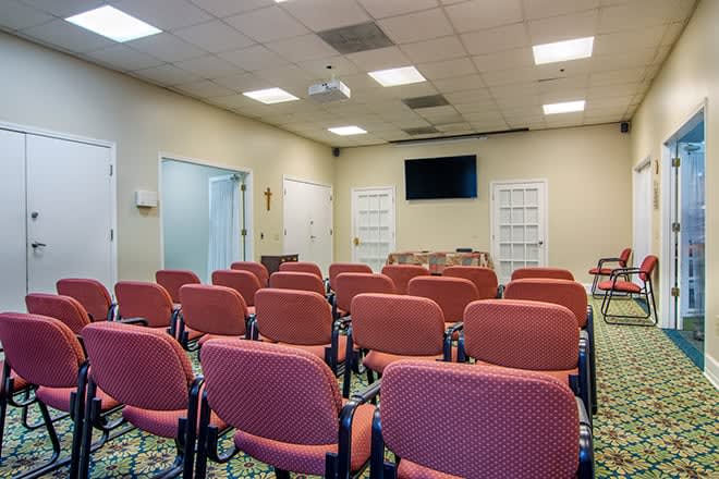 An empty conference room with rows of red chairs facing a television screen.