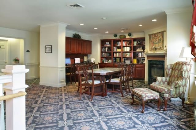 A cozy library room with bookshelves, a table, and chairs on a patterned carpet.