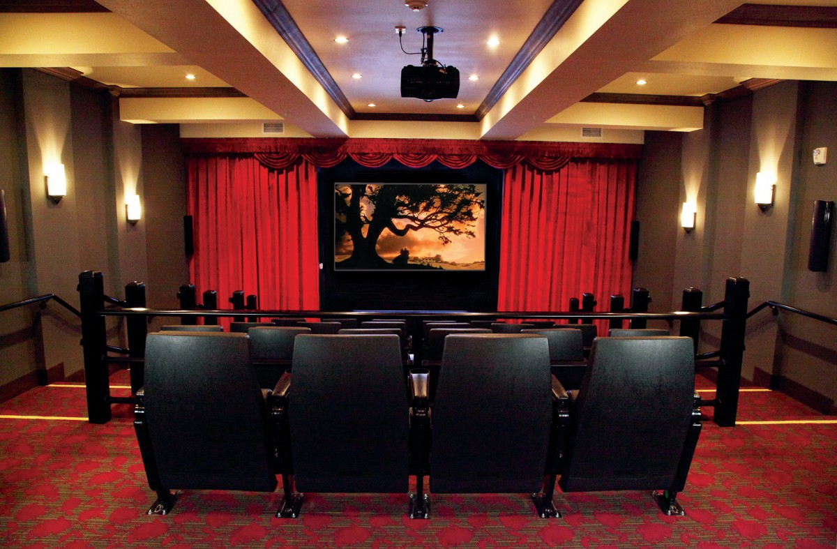 A luxurious home theater with rows of seats facing a large movie screen, framed by red curtains.