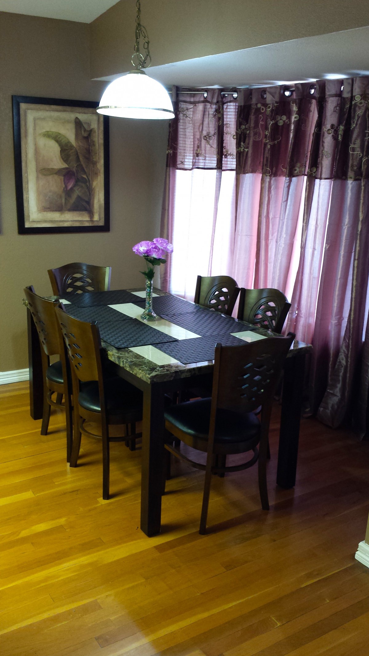 A cozy dining room with a table set for six, adorned with a vase of flowers.