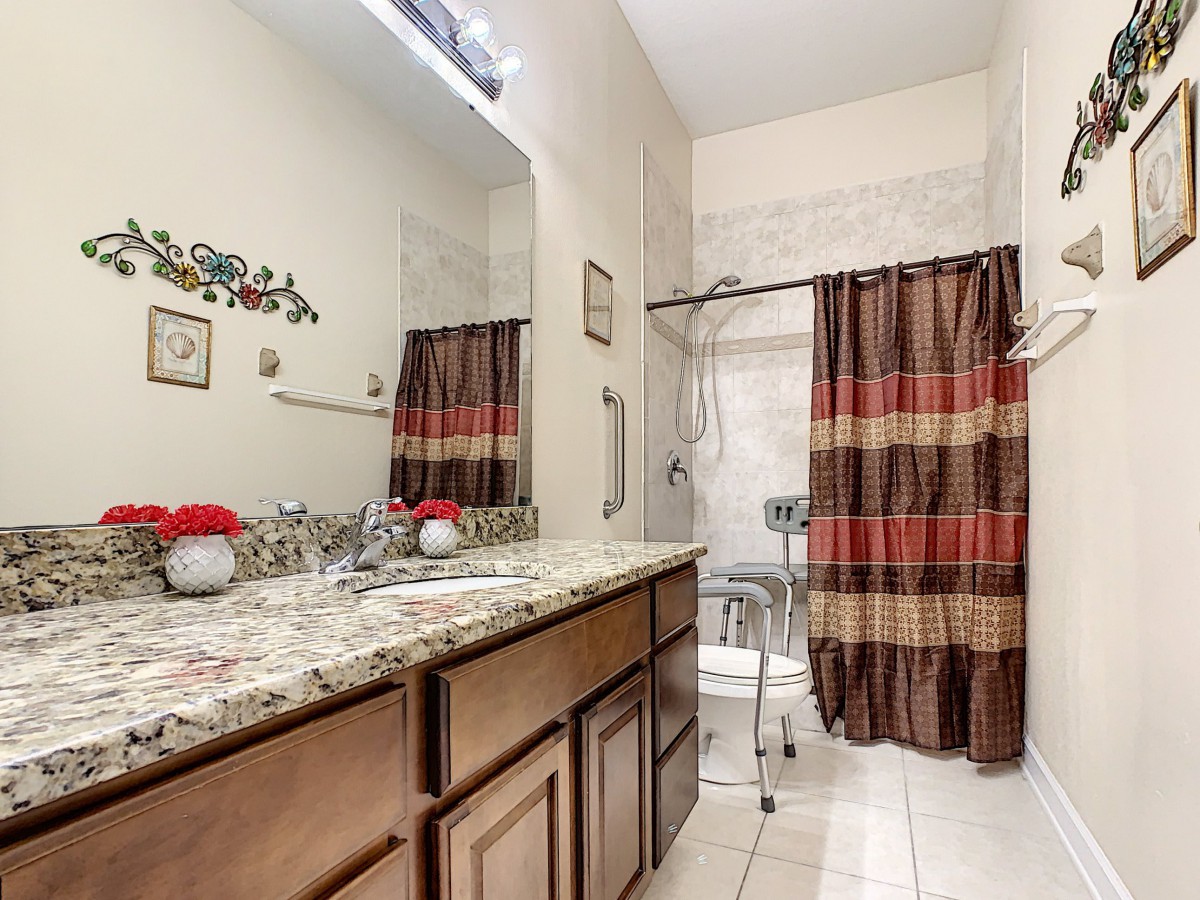 A modern bathroom with a granite countertop, large mirror, and a colorful shower curtain.