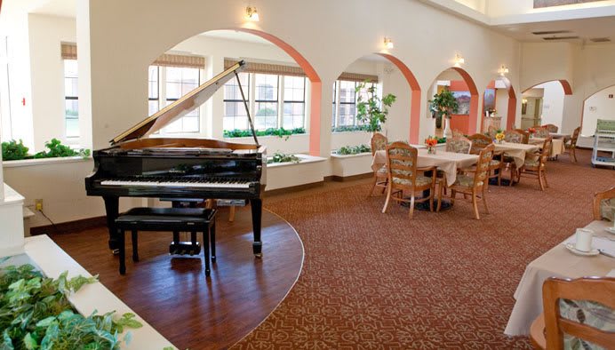 A spacious and elegant room featuring a grand piano and a dining area with arched windows.