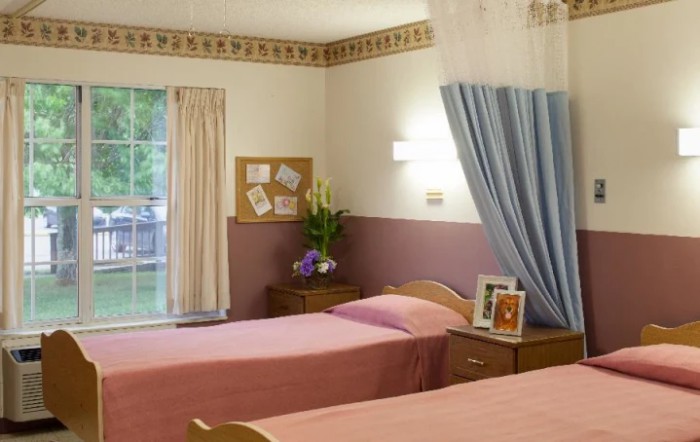 A cozy bedroom with twin beds, floral decor, and soft curtains by a window.