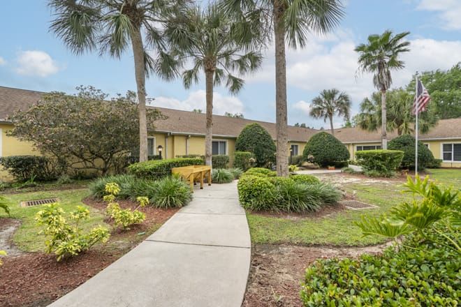 A well-maintained home with lush landscaping and palm trees lining the pathway.