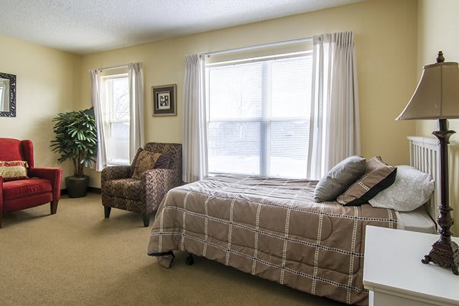 A cozy bedroom with a bed, chair, and large windows providing natural light.