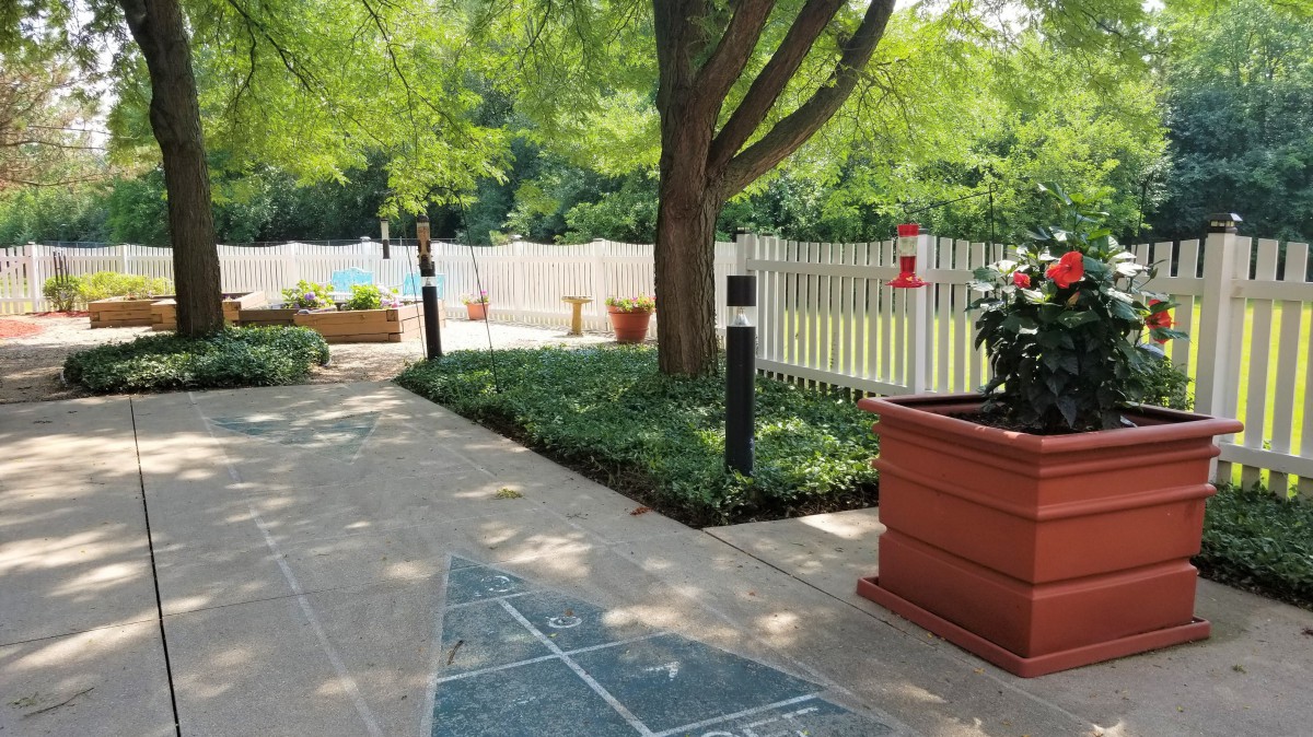 A serene garden pathway bordered by lush greenery and a white picket fence.