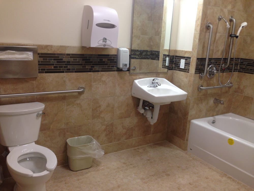 A clean, accessible bathroom with tiled walls, featuring a sink, toilet, and bathtub.
