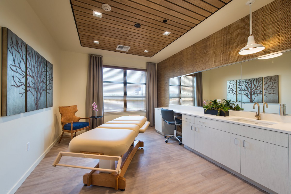 A modern massage room with a therapy table, inviting natural light through large windows.