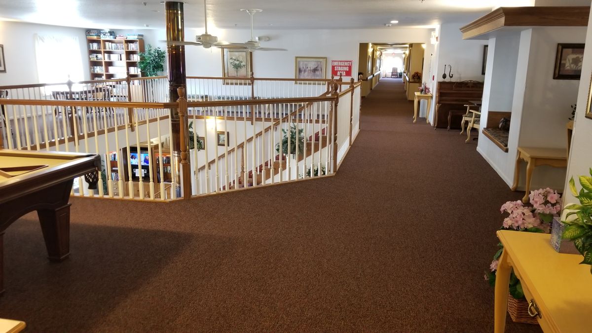 A spacious hallway with railings overlooking a staircase, featuring carpeted floors and decorative elements.