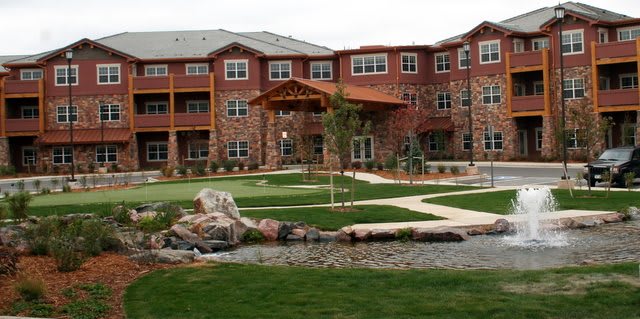 A view of a residential building with well-maintained gardens and a small pond.
