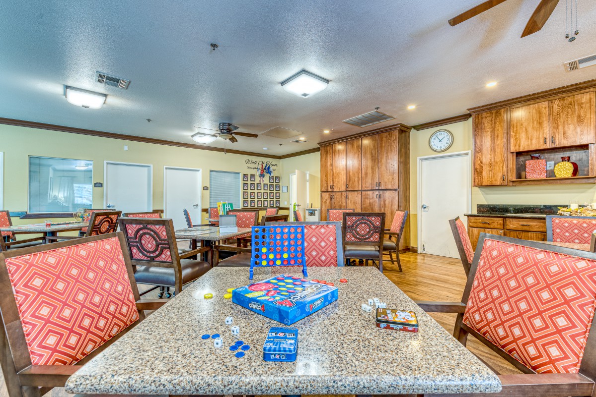 A spacious community room with tables and chairs arranged for leisure activities, featuring a Connect Four game set up on one of the tables.