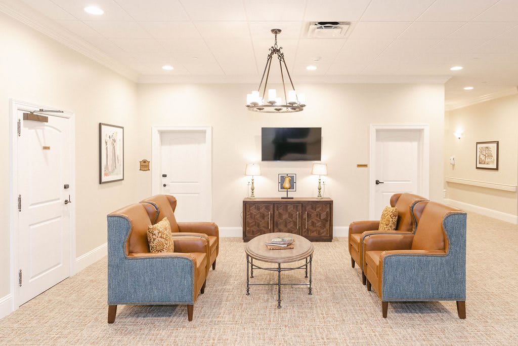 A modern living room with stylish furniture, featuring two pairs of armchairs, a central table, and a wall-mounted television.