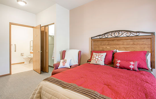 Cozy bedroom with red bedding and an armchair next to the bed.
