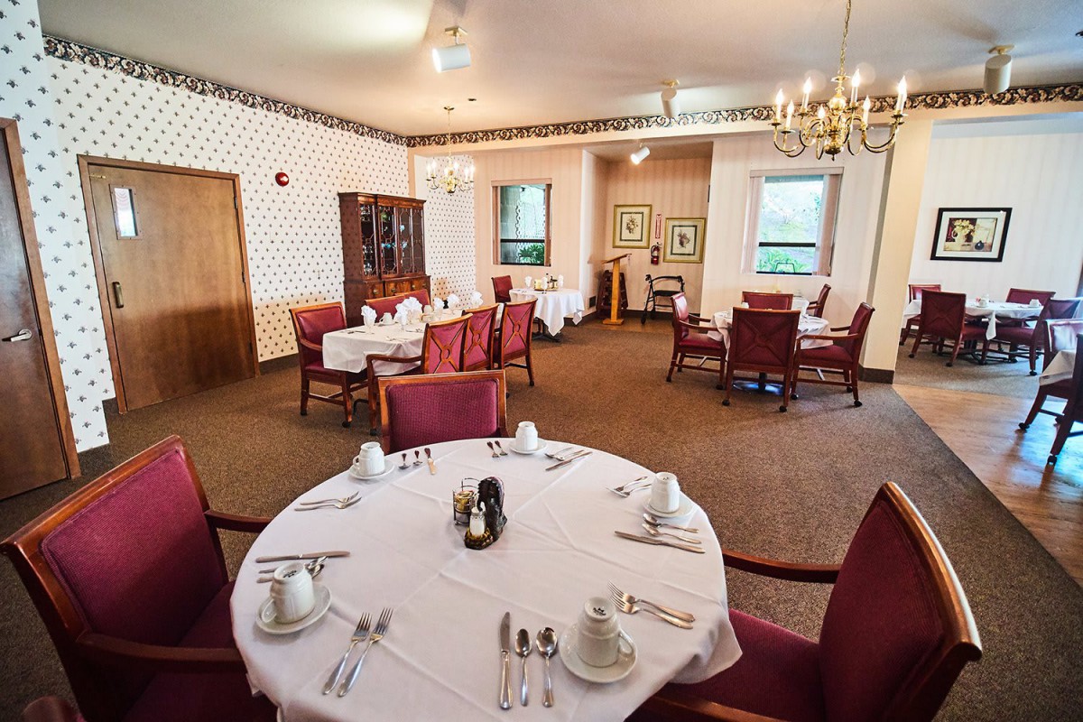 Elegantly set dining room with round tables and upholstered chairs, ready for guests.