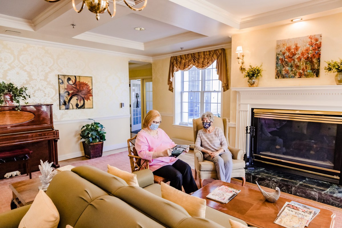 Two seniors sitting in a cozy living room with a fireplace and natural light.