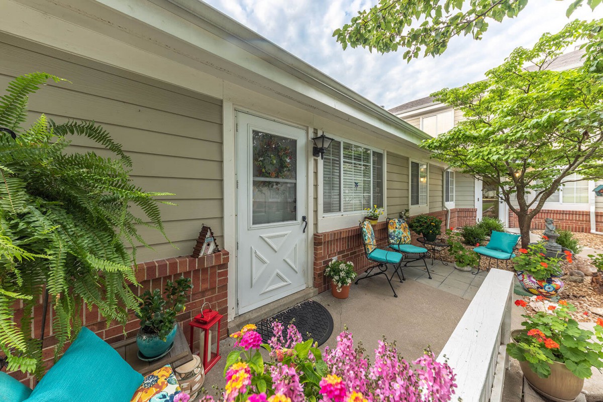 A cozy porch with colorful flowers and seating area outside a house.