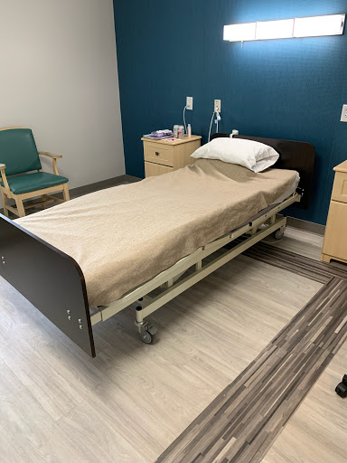 A hospital room featuring a patient bed, bedside tables, and a chair.