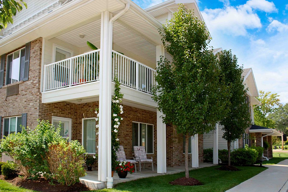 A modern house with a balcony and porch, surrounded by a garden and trees.
